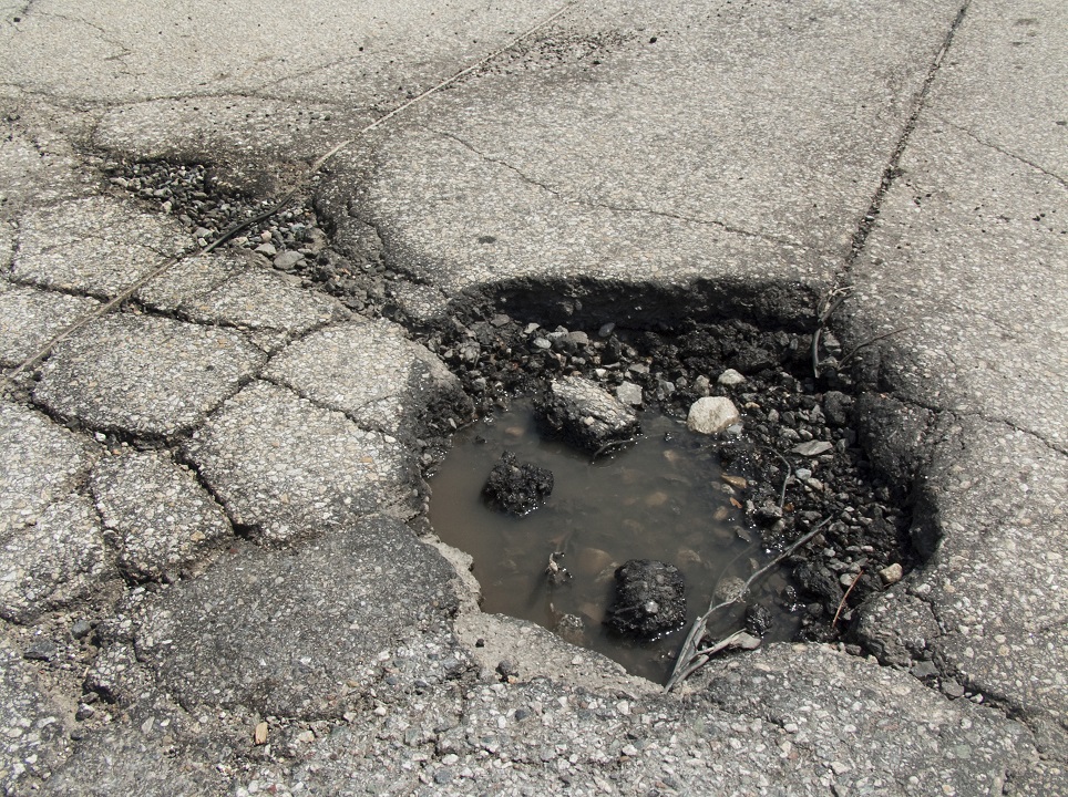 720-pothole-repair Large pothole filled with water and debris on a cracked asphalt road surface.