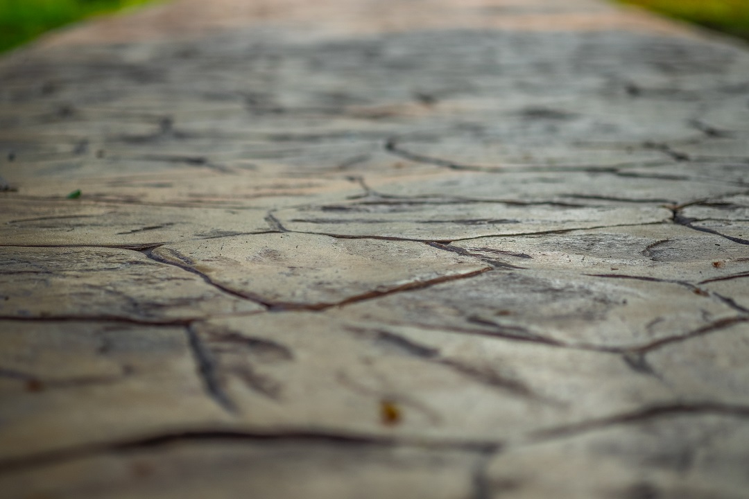 Close up view of walkway concrete stamped material, selective focus. Close-up of a stone walkway with irregular patterns, blurred greenery in the background.