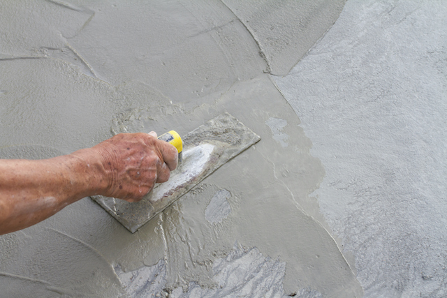 ThinkstockPhotos-184704964 Hand using a trowel to smooth wet cement on a surface.