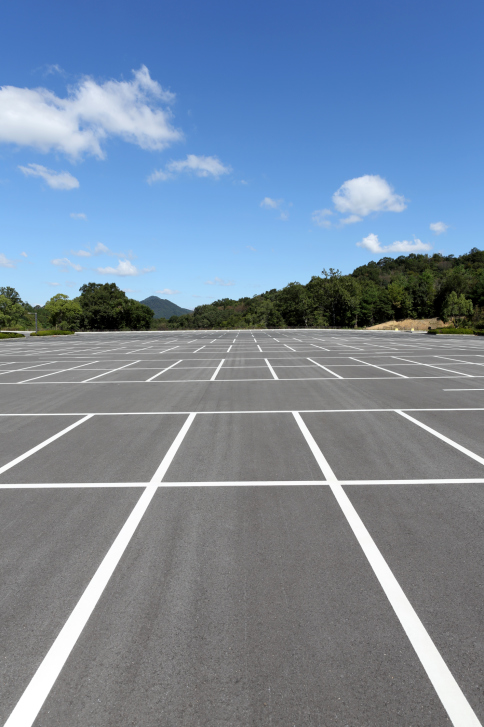 ThinkstockPhotos-492491566 Empty parking lot with white lines under a blue sky and surrounded by trees and distant hills.