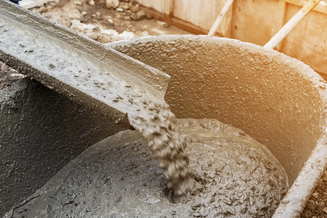 asphalt-b Wet concrete pouring from a chute into a large mixing container at a construction site.