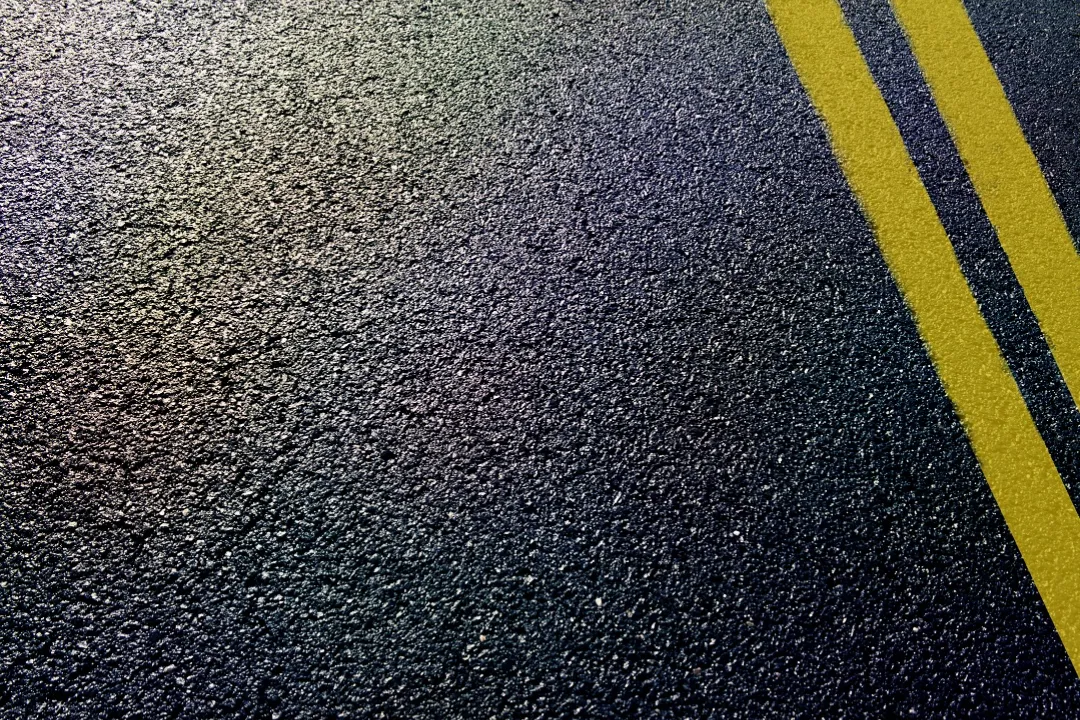 asphalt-b2 Close-up of dark asphalt with two parallel yellow road lines running diagonally on the right side.