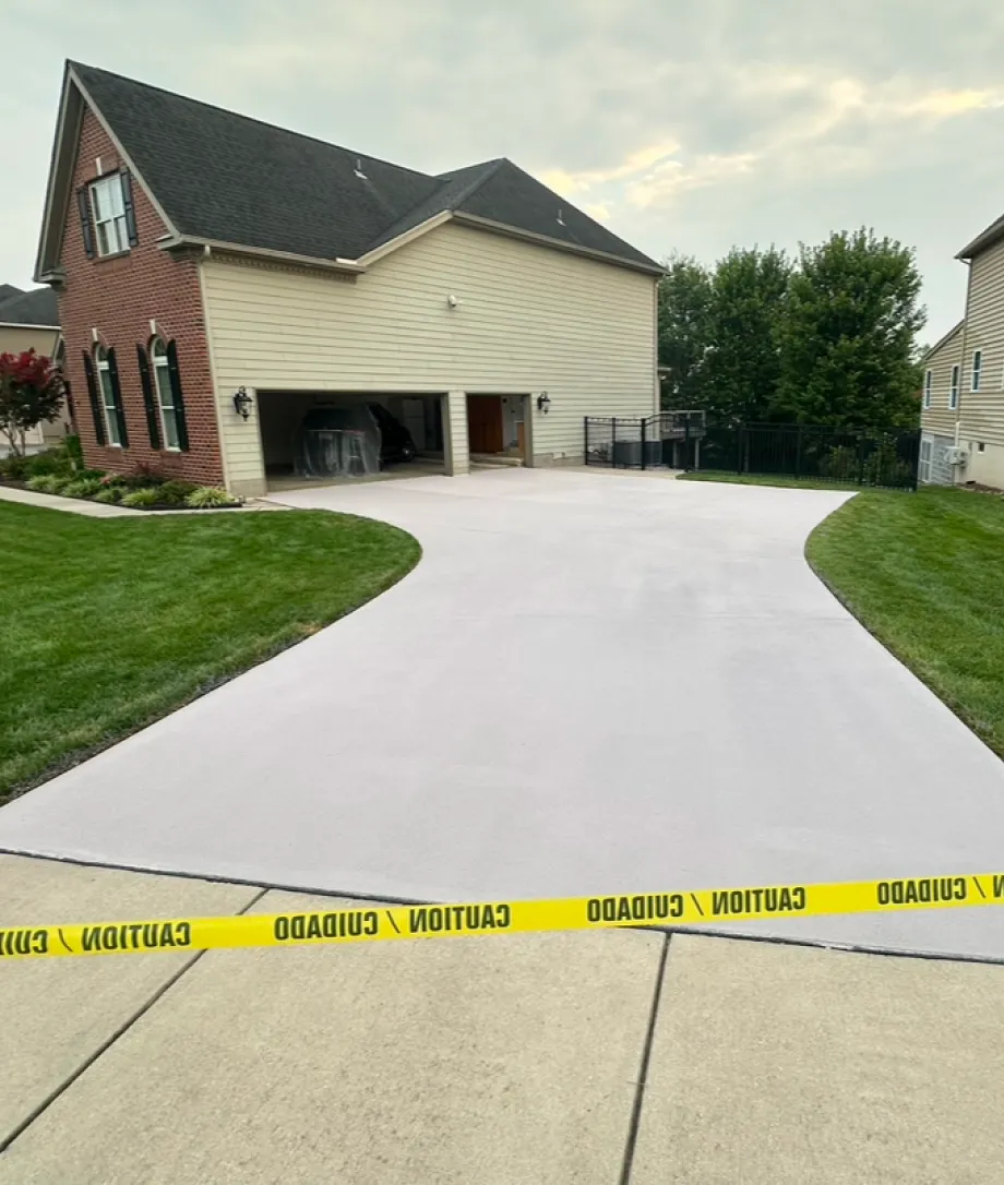 Freshly paved driveway with caution tape blocking it, in front of a two-story suburban house.