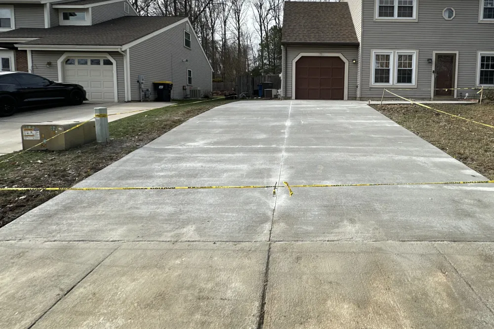 Freshly poured concrete driveway roped off with yellow tape in front of a suburban house.