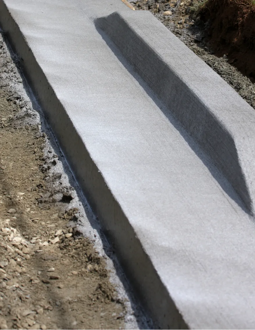 Freshly poured concrete curb beside dirt, showing a smooth finish and a distinct angled groove.