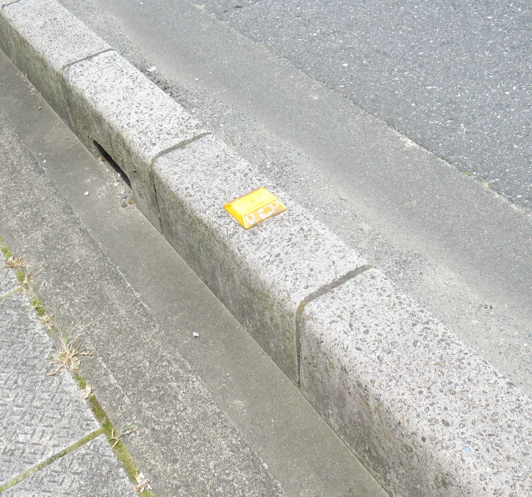 A yellow cassette tape lies on a concrete curb beside an asphalt road.