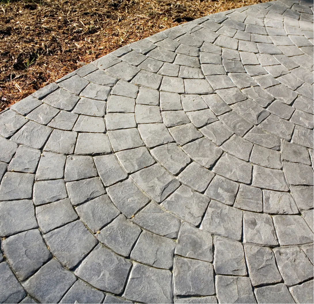 Curved stone pavement with a fan pattern next to a mulched dirt area.
