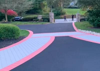A black driveway with red borders and two people standing near stone pillars at the entrance.