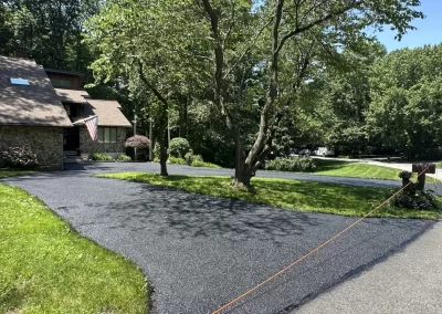 A driveway with fresh asphalt is blocked by orange tape; trees and a house with an American flag nearby.