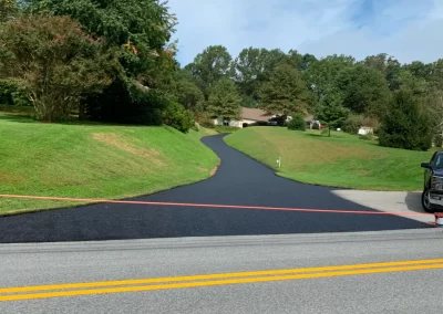Freshly paved black driveway leading uphill to a house, with a red rope blocking access at the road.