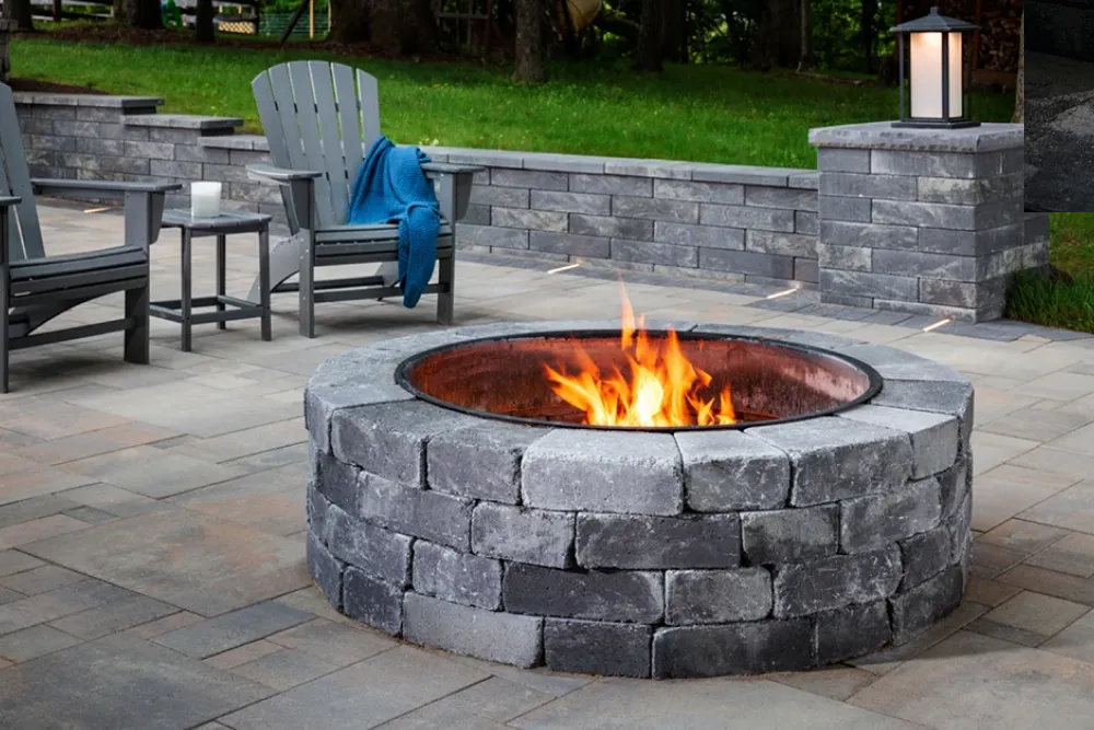 Round stone fire pit with burning fire, surrounded by patio chairs and a gray stone patio.