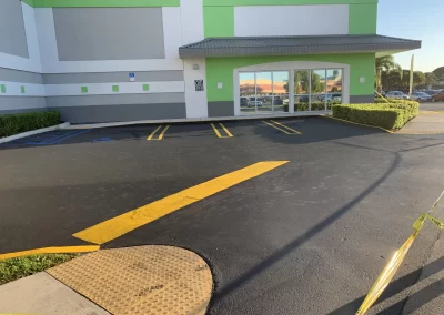 Accessible parking spaces and yellow caution tape near a building with glass doors, sunny day.