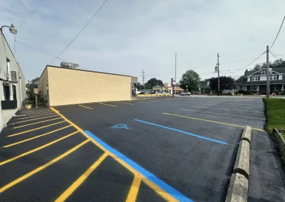 Freshly paved empty parking lot with yellow lines and a blue accessible parking space near a beige building.