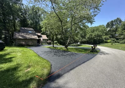 Freshly paved driveway with an orange rope blocking entry, beside a house surrounded by green trees.