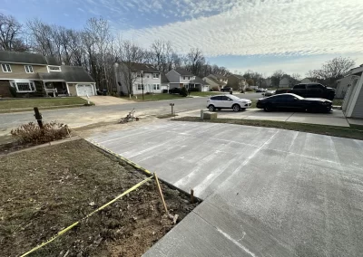 Freshly paved driveway in a suburban neighborhood, with cars parked and yellow caution tape on the side.