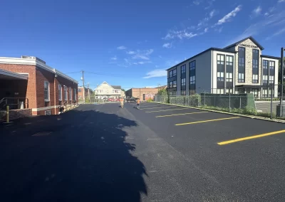 A newly paved parking lot with two people walking toward the back, between a brick building and Commerce Corner.
