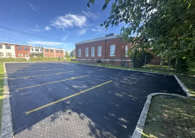 Freshly paved empty parking lot beside a red brick building, with trees casting shadows.