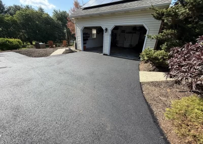 Freshly paved asphalt driveway leading to a two-car garage with open doors, garden visible around.