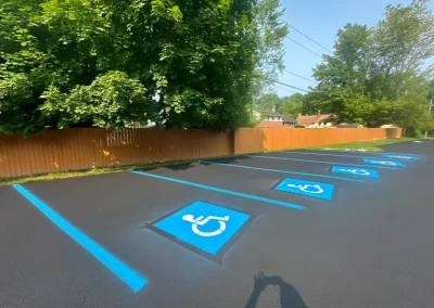 Four freshly painted accessible parking spaces with blue wheelchair symbols on black pavement near a wooden fence.
