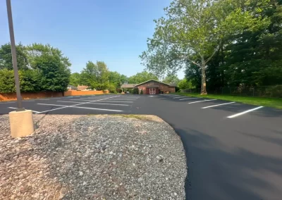 Freshly paved, empty parking lot with white lines, trees, and a brick building in the background.