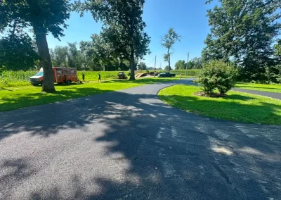 Curved paved path in a sunny park with trees, grass, and a red food truck on the left.