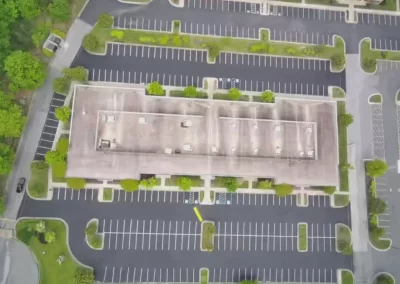 Aerial view of an empty parking lot surrounding a rectangular building with trees and bushes nearby.