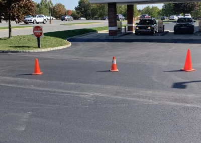 Three orange traffic cones block a freshly paved entrance near a "Do Not Enter" sign at a drive-thru.