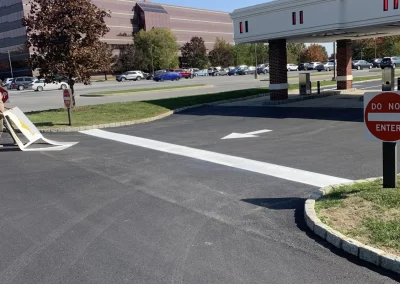 Driveway with "Do Not Enter" signs, white arrow painted on road, office building and parked cars in background.