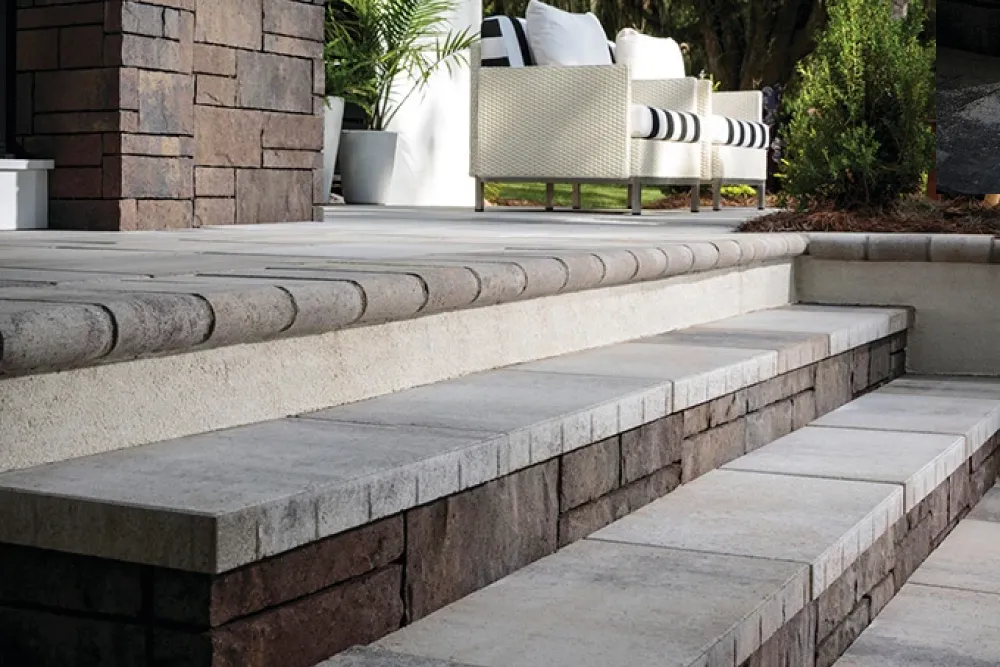 Stone steps leading up to a patio with outdoor seating and green plants in the background.