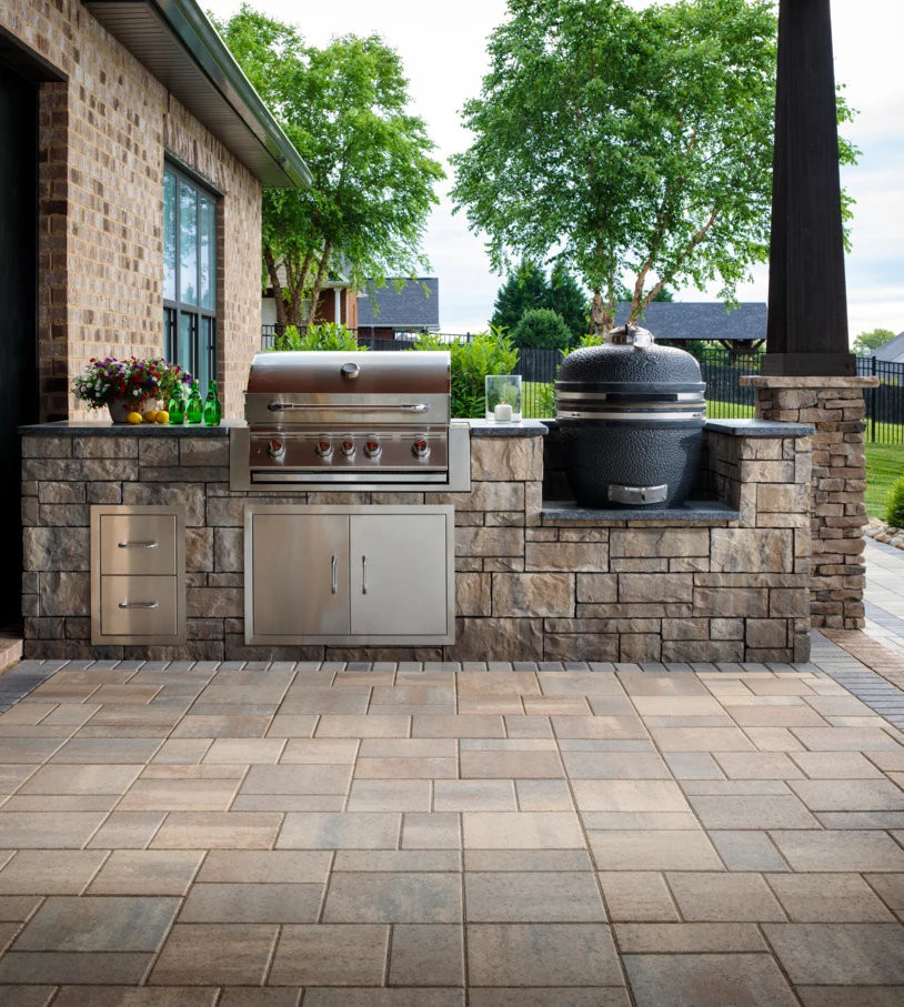 Outdoor patio kitchen with built-in gas grill, smoker, stone countertop, and paver flooring.
