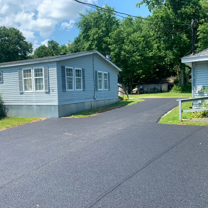 Freshly paved black asphalt driveway between two light blue houses with green trees in the background.