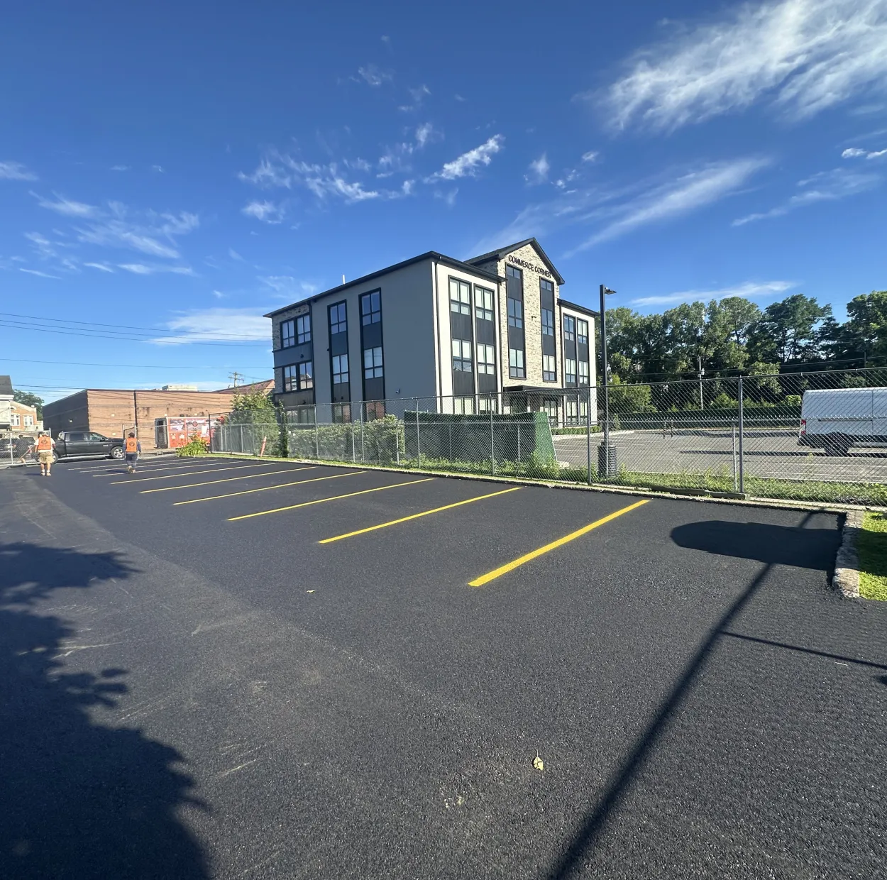 A modern three-story building beside a freshly paved, mostly empty parking lot under a blue sky.