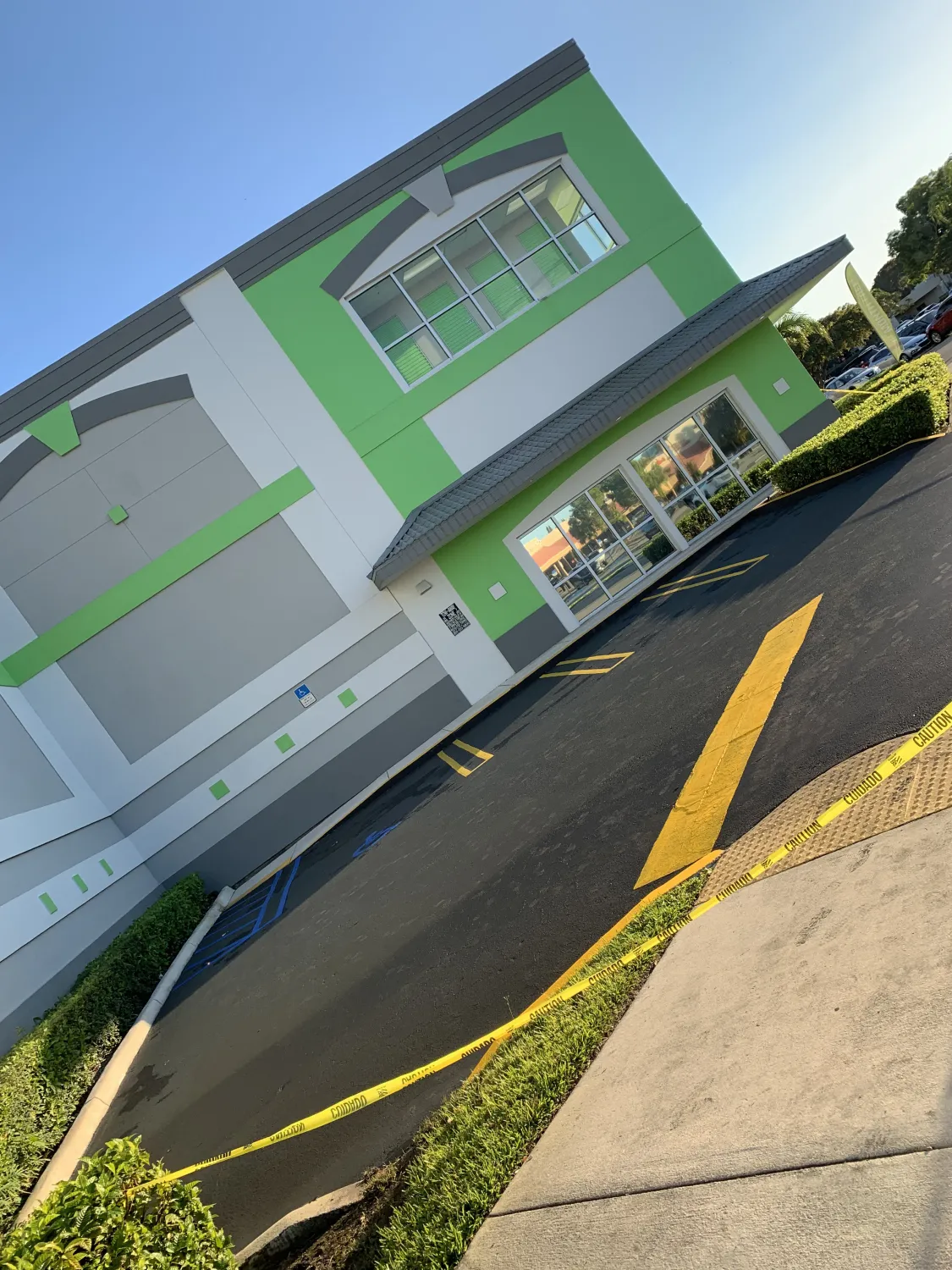 A green and white building with caution tape blocking part of the parking lot and a yellow arrow on pavement.