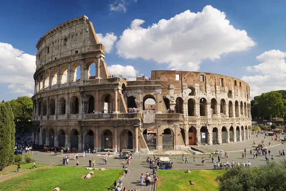 The Roman Colosseum with tourists walking around on a sunny day, blue sky and clouds above.