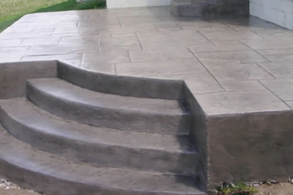 Four curved concrete steps lead up to a patterned concrete porch with grass visible on the side.
