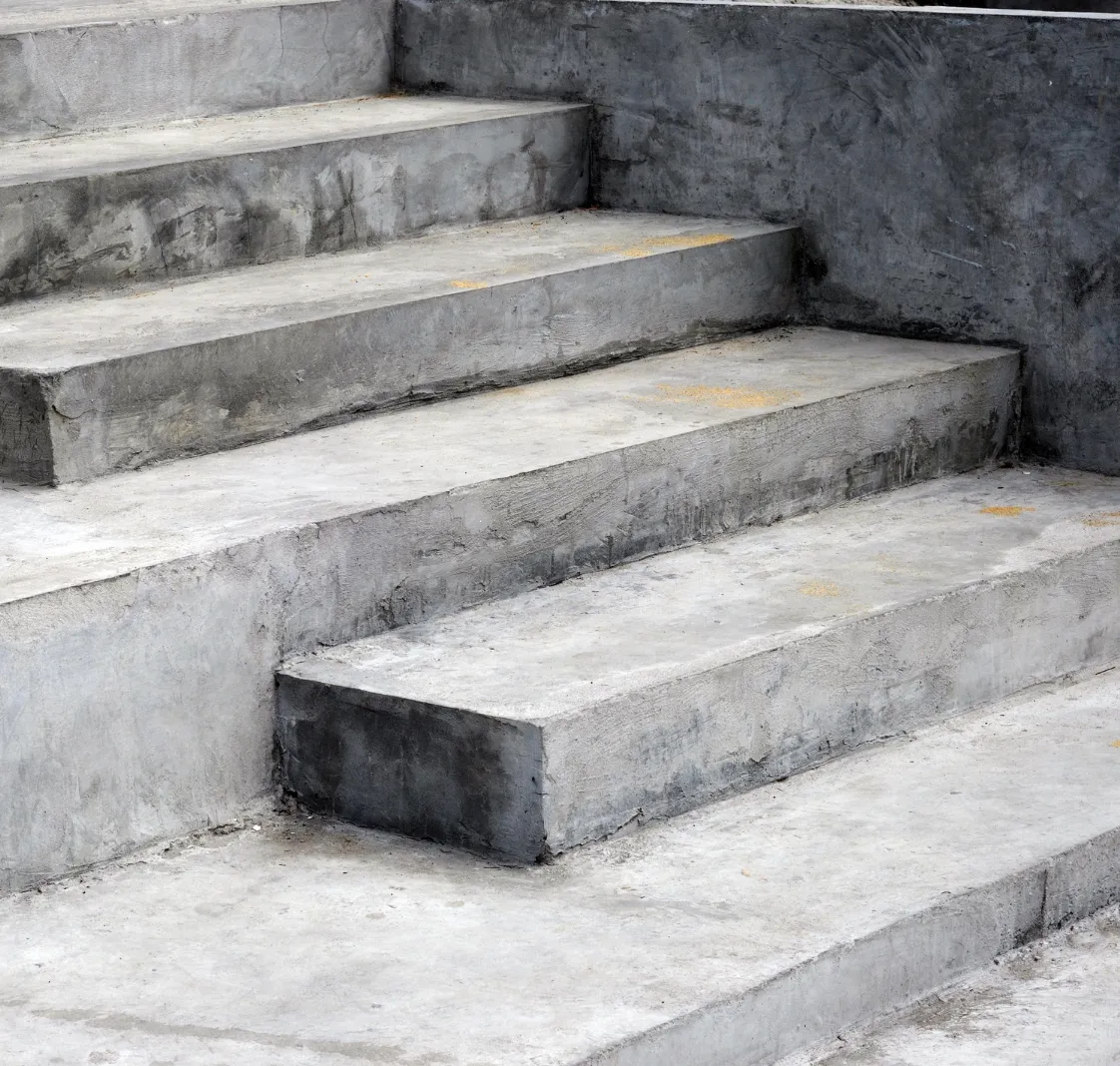 Concrete stairs with uneven steps and rough surfaces, bordered by a low concrete wall.