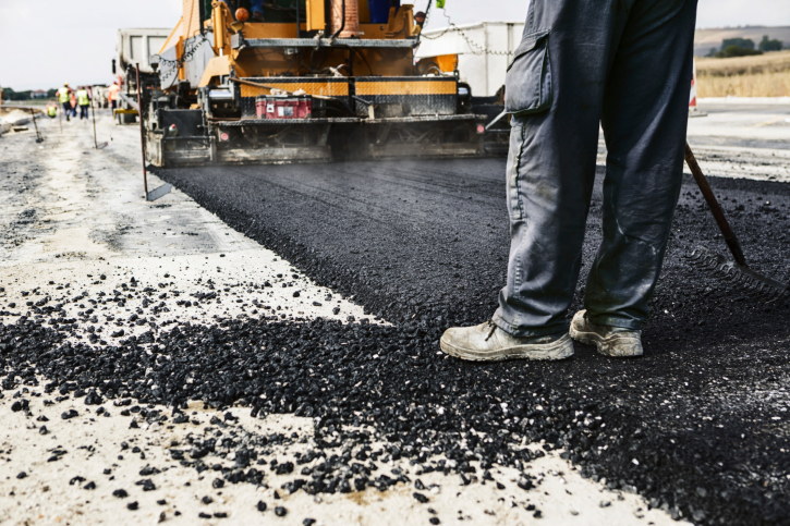 ThinkstockPhotos-469577715 Workers paving a road with fresh asphalt; one worker stands in the foreground near paving machinery.