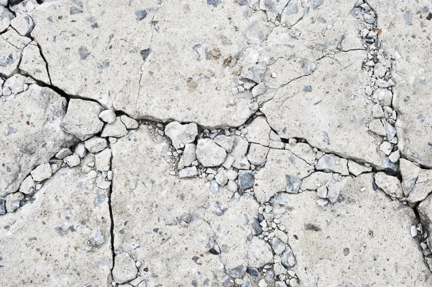image 1 Cracked concrete surface with visible jagged lines and scattered small loose stones.