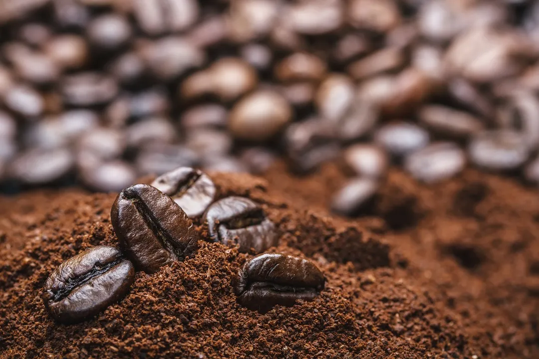 image 2 Coffee beans resting on a pile of ground coffee, with more beans blurred in the background.